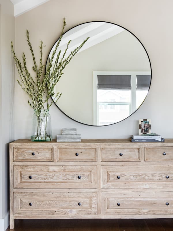 Round wall mirror above rustic wooden dresser