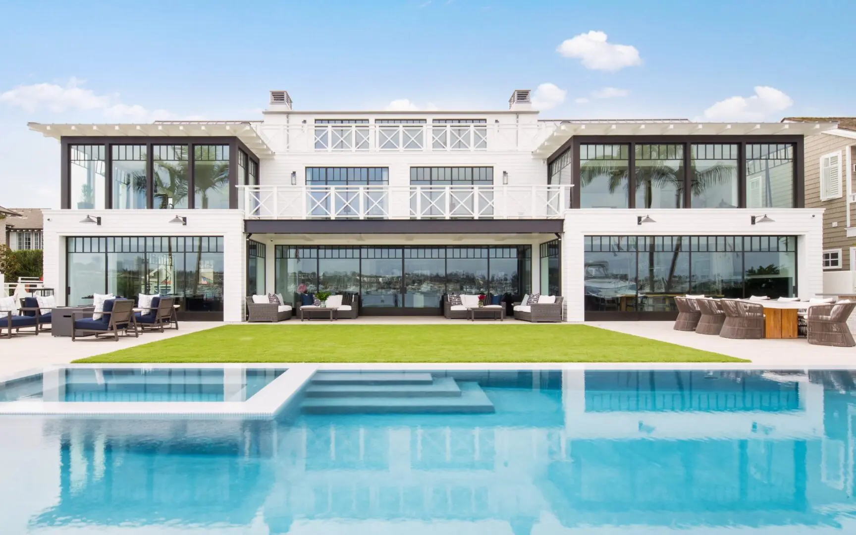 Large white and black modern farmhouse with an infinity edge pool on the bay of Newport Harbor.