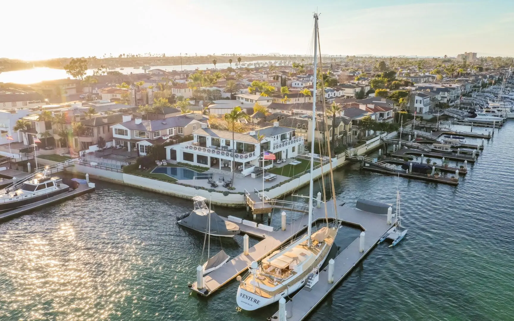 Aerial view of a white coastal home and luxury sailing yacht on Newport Harbor.