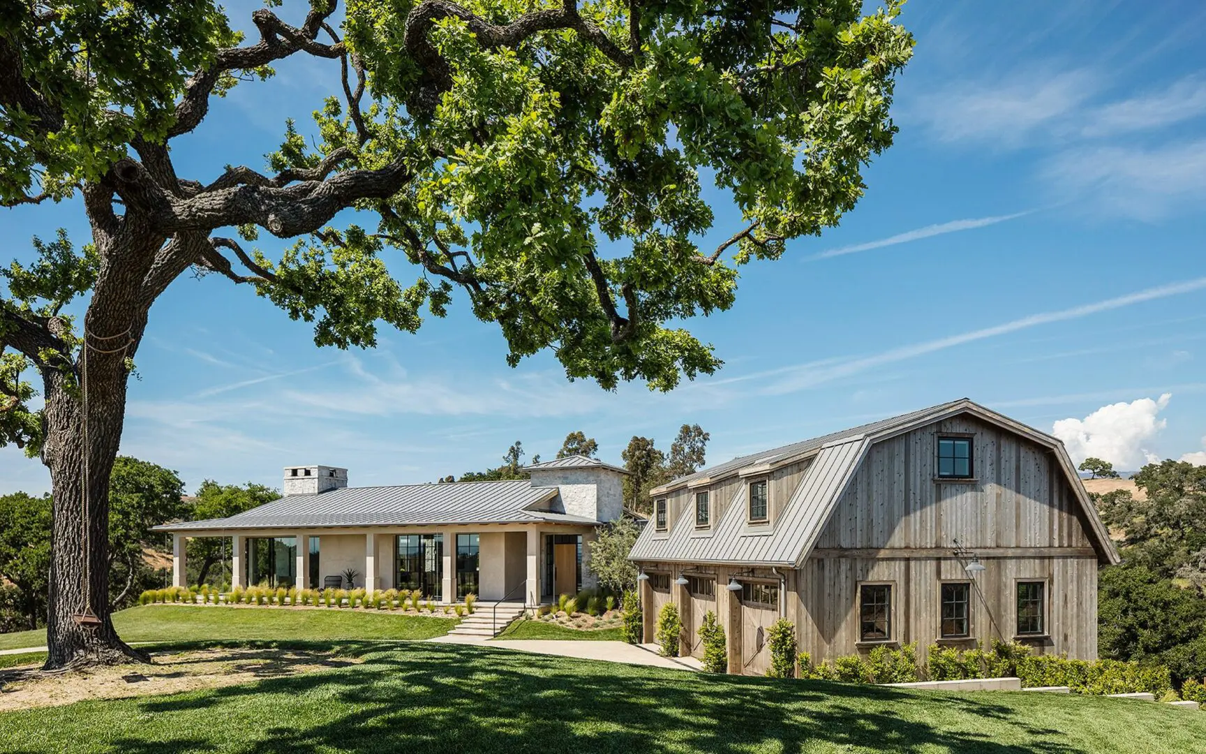 Ranch-style home and carriage house perched on rolling hills around a large oak tree.
