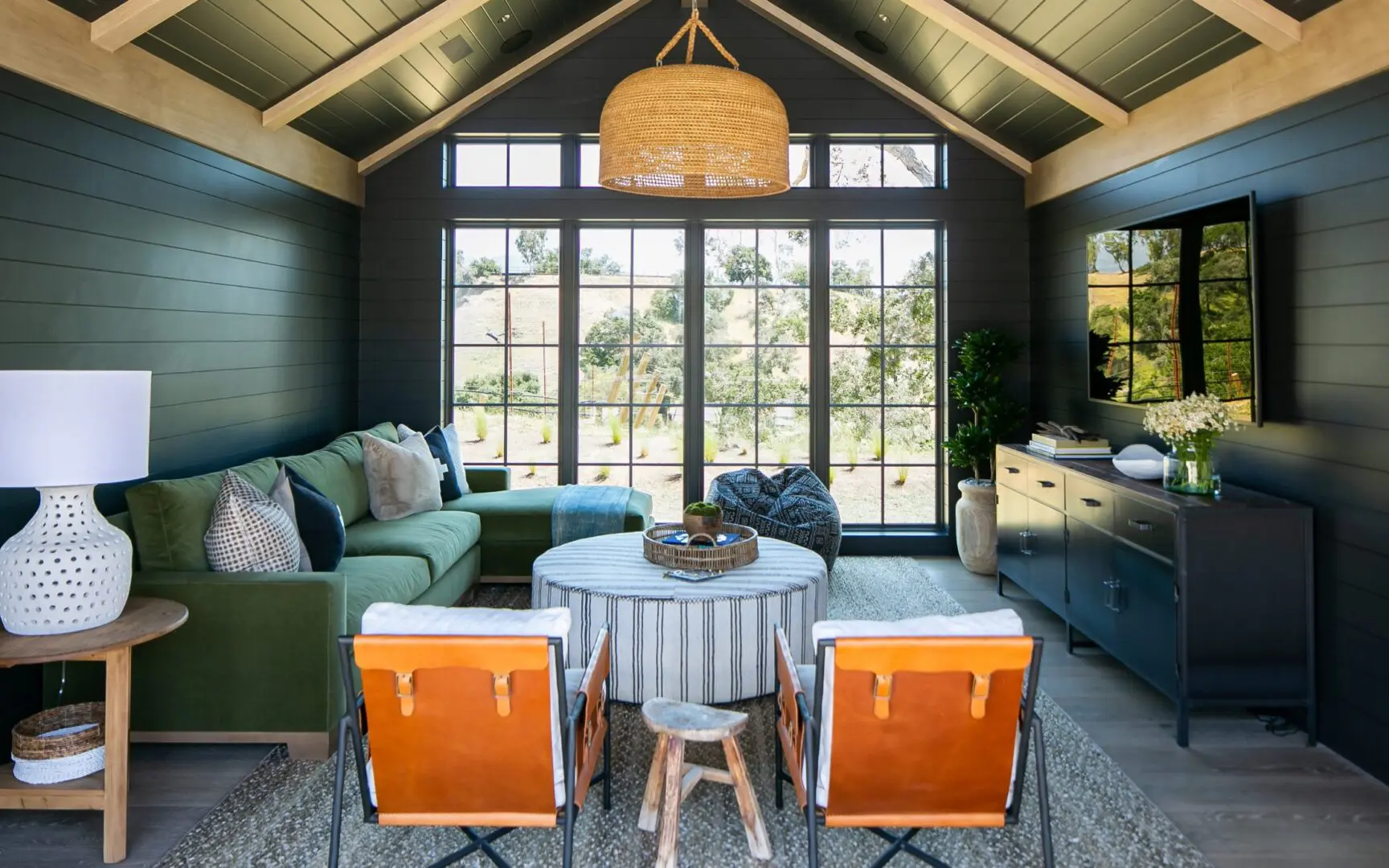 Moody family room with black paneled walls, green sectional sofa, and leather saddle chairs.