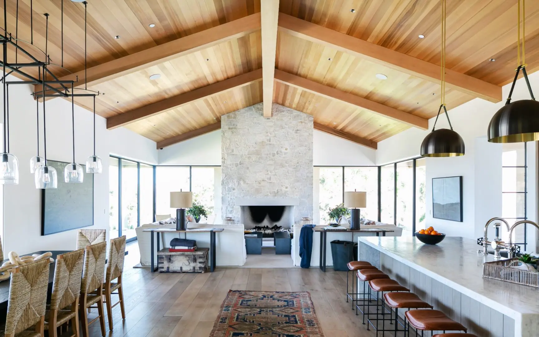 An open concept great room in a ranch-style home with stone fireplace, wood ceilings, and custom furniture.
