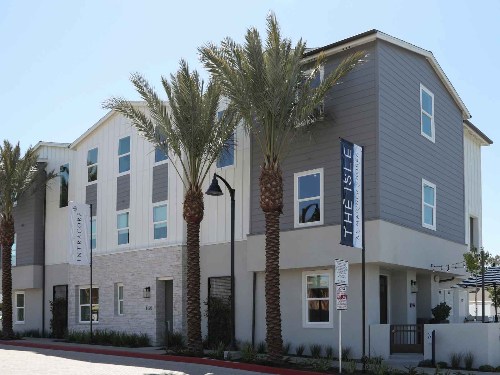 Gray and white modern farmhouse townhomes with palm trees and light posts.