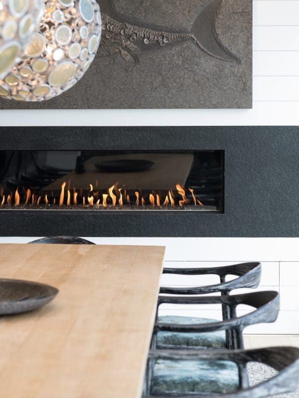 blackband-design-newport-waterfront-dining-fireplace Linear fireplace and fossil art next to a dining table.
