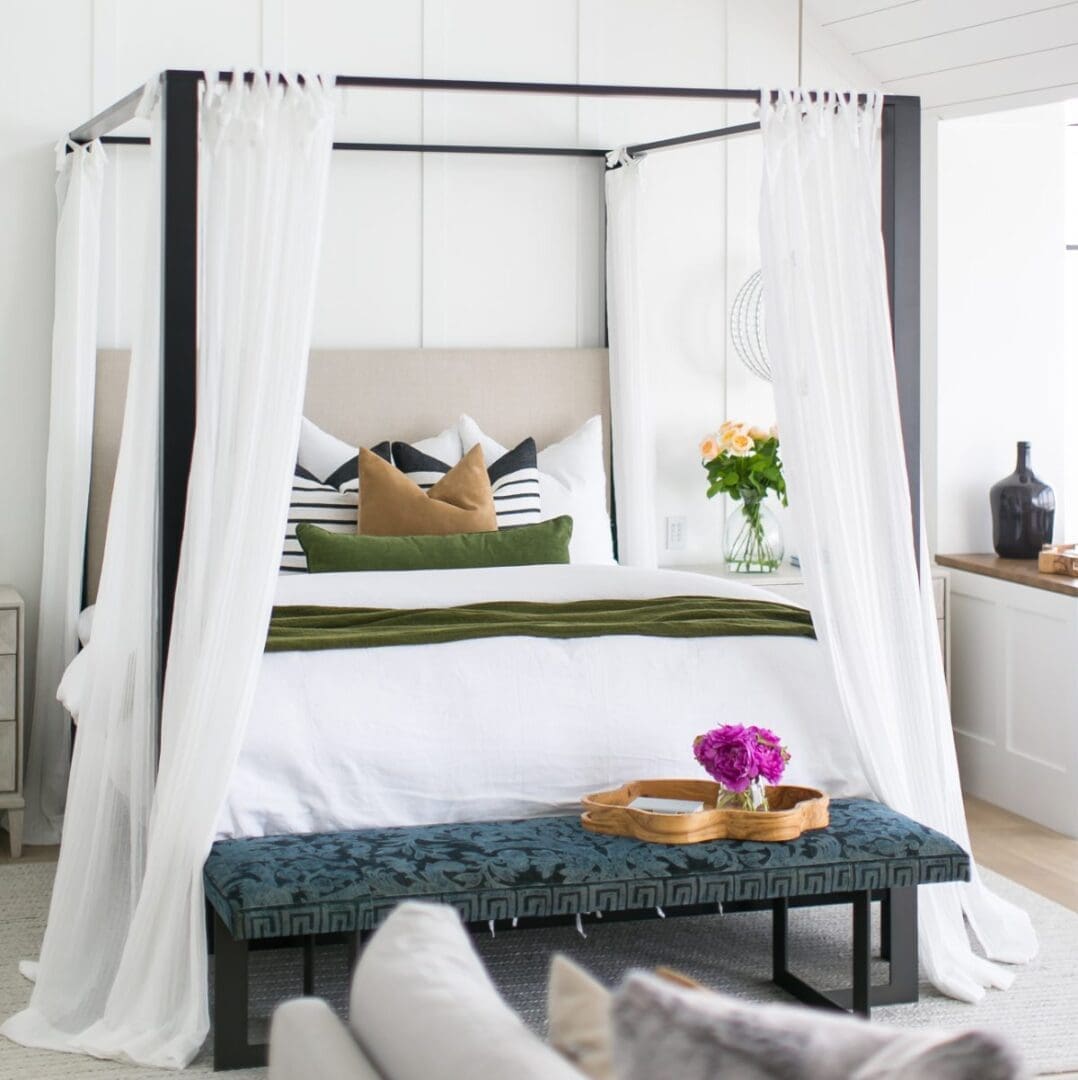 Canopy bed with white linens and a blue velvet bench.